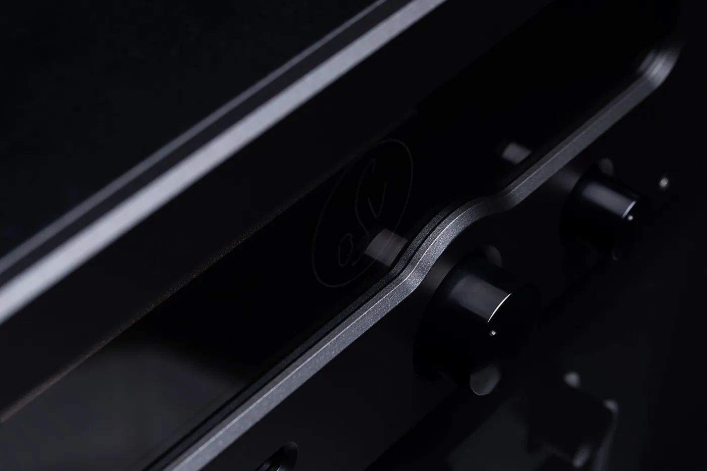The sculpted front rail of an OSV Audio amplifier in raking light, the etched monogram beside the volume control
